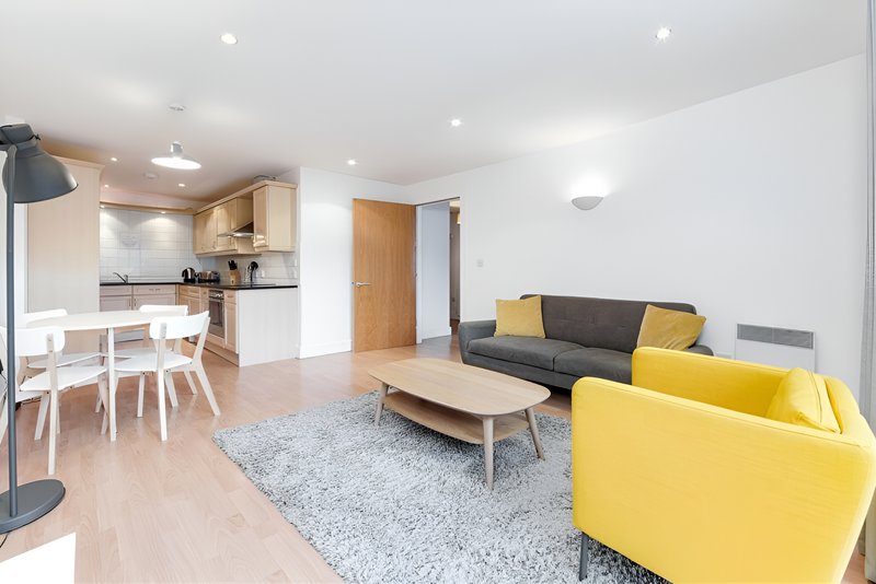 Open-plan living room with yellow armchair, grey sofa, wooden table and kitchen area
