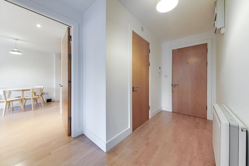 Bright hallway with wooden floors, white walls, brown doors, and radiator
