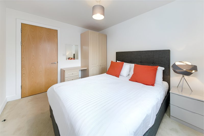 Modern bedroom with double bed, grey headboard, orange pillows, wooden door and built-in wardrobe