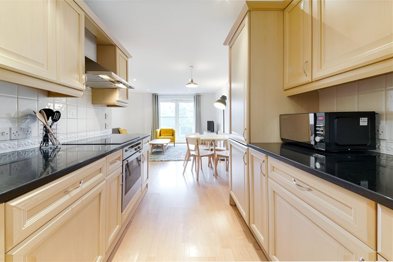 Galley kitchen with cream cabinets, black countertops, and dining area beyond