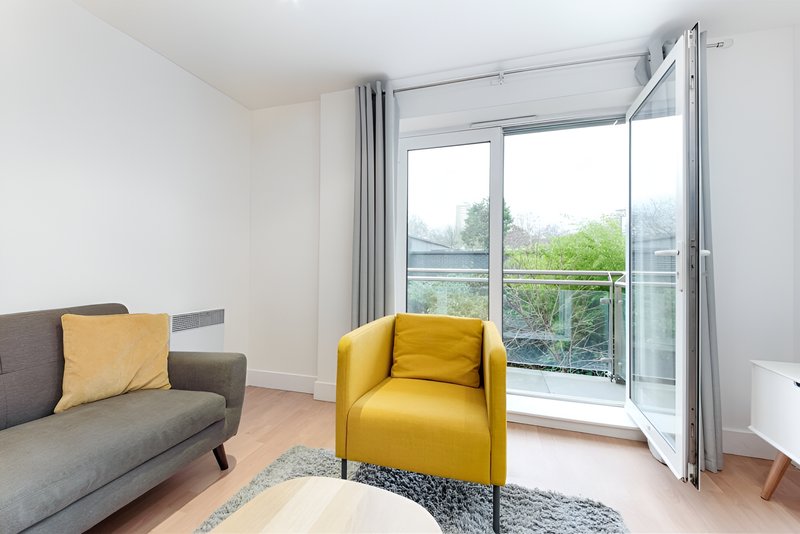 Modern living room with gray sofa, yellow armchair, and glass doors overlooking garden