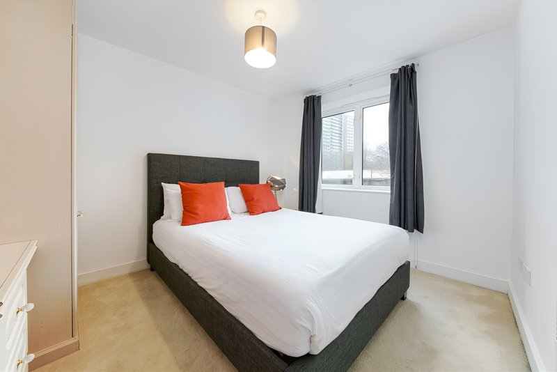 Modern bedroom with dark bed frame, white bedding, orange cushions and window with dark curtains