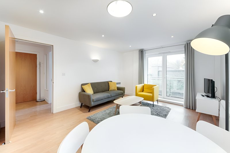 Modern studio apartment with bed, gray sofa, yellow chair, and floor-to-ceiling windows