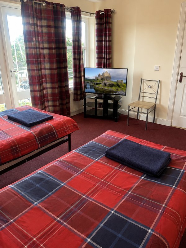 Bedroom with two single beds, tartan bedding, TV on stand, plaid curtains and window view