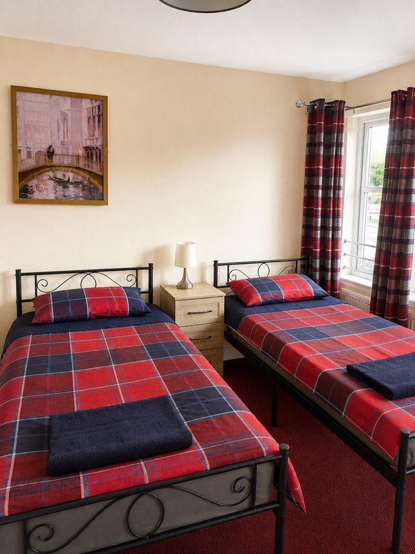 Twin bedroom with red tartan bedding, metal frame beds, cream walls and plaid curtains