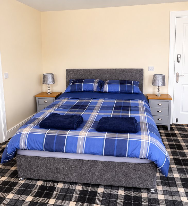 Bedroom with double bed, blue plaid bedding, grey headboard, wooden nightstands with lamps