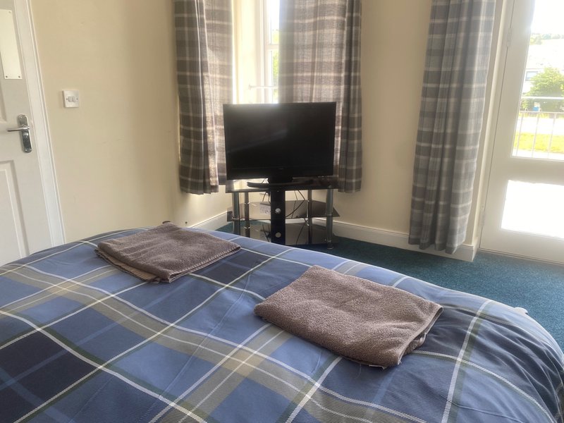 Bedroom with double bed, plaid bedding, TV on stand, plaid curtains and patio doors