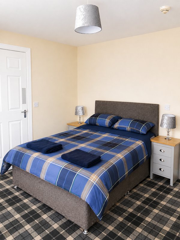 Bedroom with double bed, blue plaid bedding, grey headboard, wooden nightstands and ceiling lamp