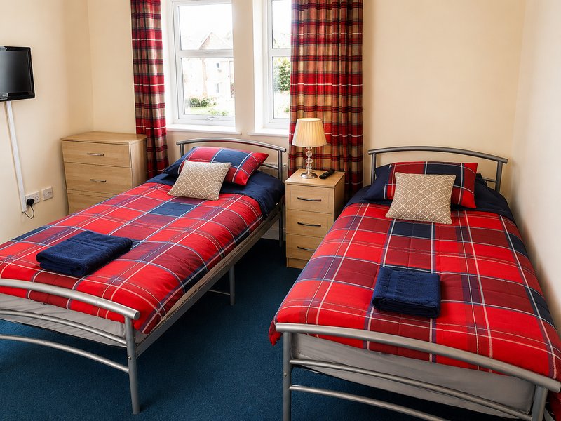 Bedroom with two single beds, red tartan bedding, wooden furniture and window with red curtains