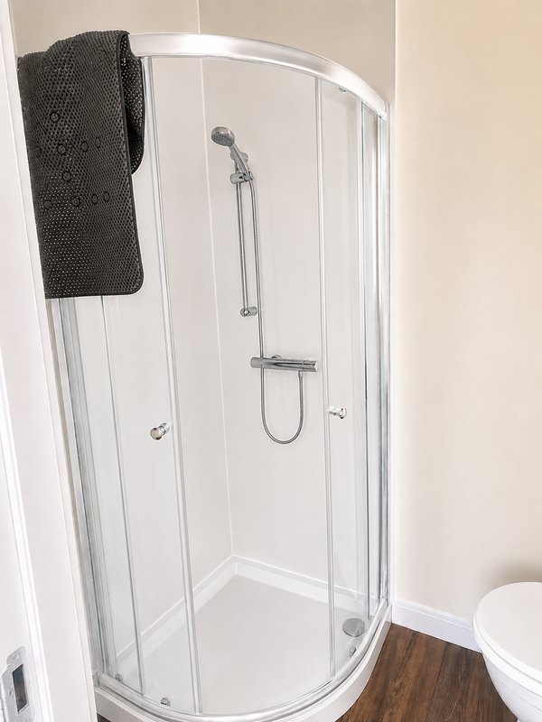 Modern bathroom with curved glass shower enclosure, chrome fixtures and dark towel rail
