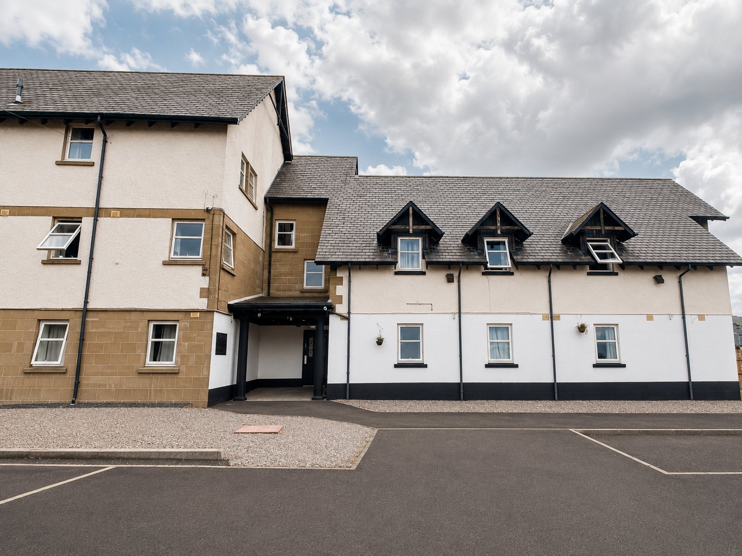Multi-story residential building with mixed cream and stone facade, dormer windows, and paved driveway