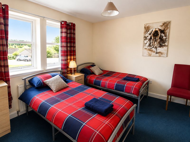 Bright bedroom with two single beds, red tartan bedding, plaid curtains, and countryside view from window