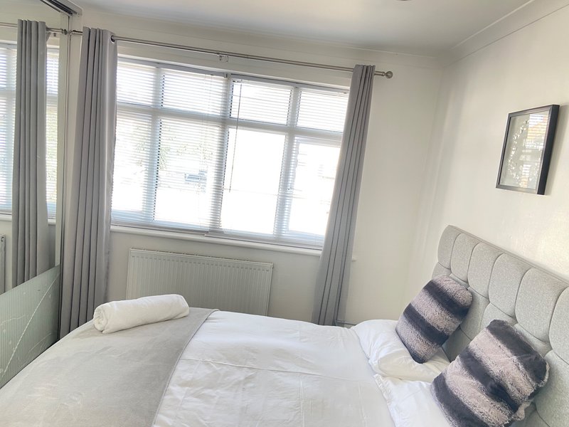 Bright bedroom with double bed, striped cushions, large window and grey curtains