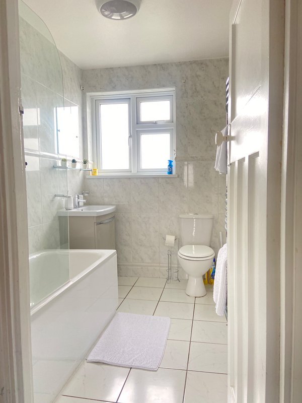 Clean bathroom with bathtub, toilet, sink, window and tiled flooring