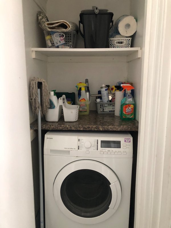 Laundry closet with white washing machine, shelves storing cleaning supplies and household items