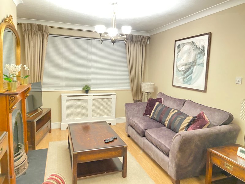 Living room with purple sofa, wooden coffee table, window with cream curtains and framed wall art