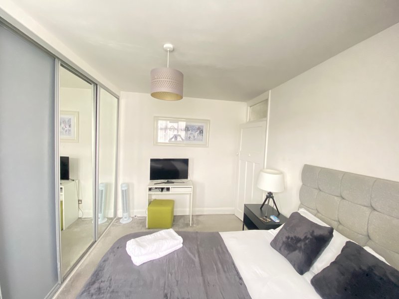 Modern bedroom with double bed, grey headboard, TV on white dresser, and mirrored wardrobe
