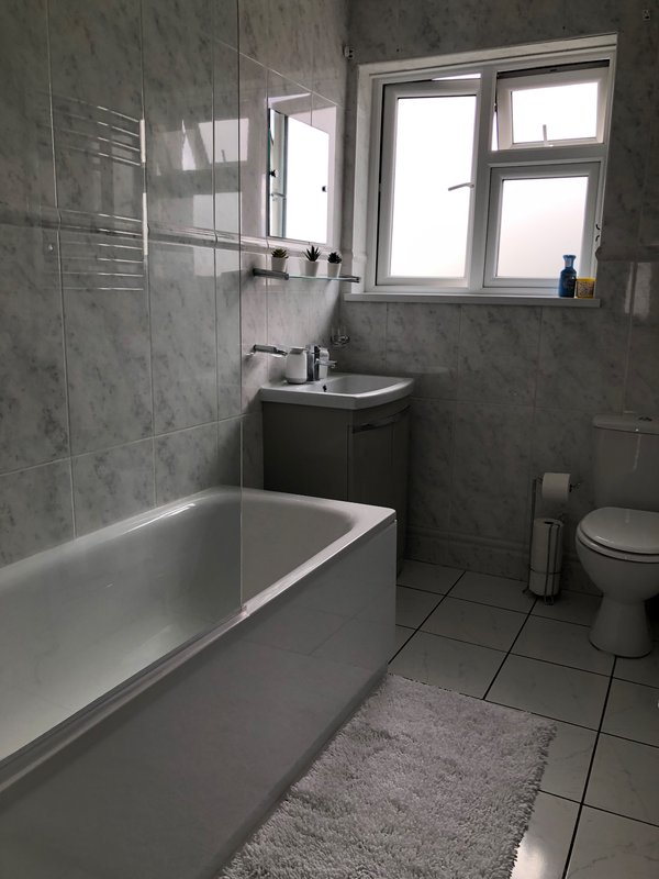 Modern bathroom with bathtub, sink vanity, toilet, window and grey tile walls