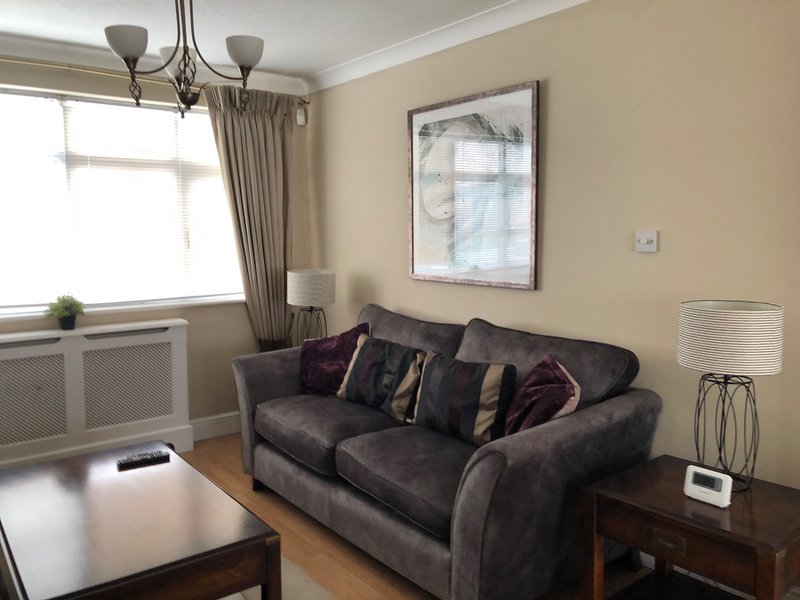 Living room with dark grey sofa, wooden coffee table, window with beige curtains and wall art