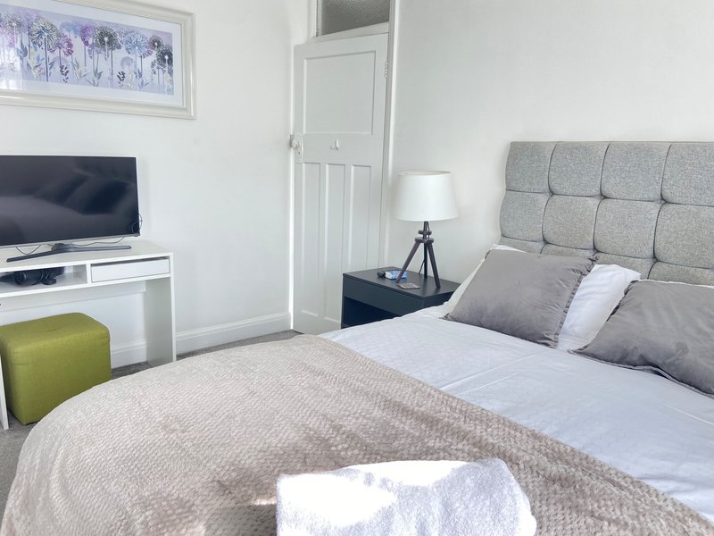 Modern bedroom with double bed, gray upholstered headboard, bedside lamp and TV on wall