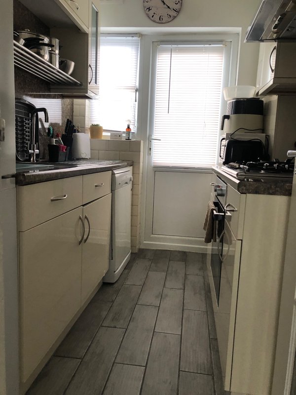 Narrow galley kitchen with cream cabinets, black countertops, gas cooker and window