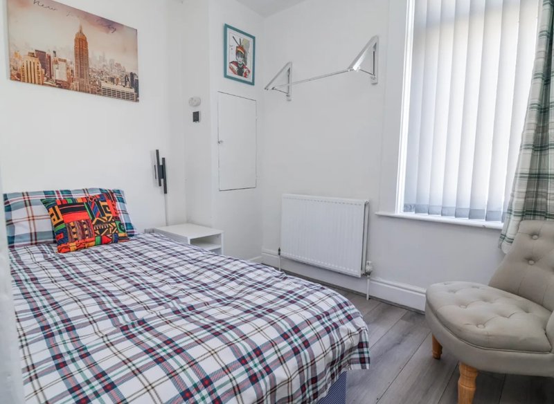 Bright bedroom with single bed, plaid bedding, upholstered chair, and vertical blinds