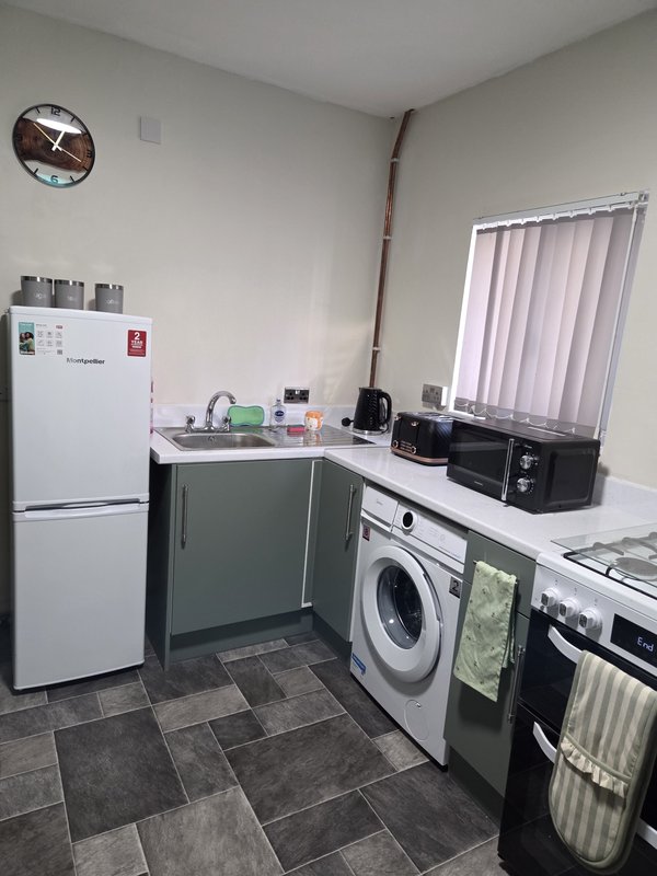 Kitchen with white fridge, washing machine, sink, countertop appliances and wall clock