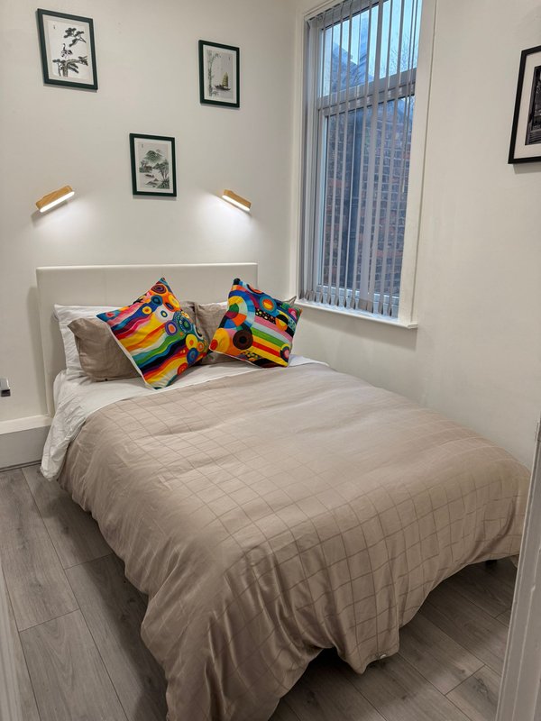 Bright modern bedroom with double bed, colorful cushions, wall art, and vertical blinds