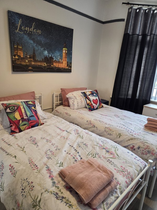 Twin bedroom with floral bedding, colorful cushions, London cityscape wall art, and black curtains