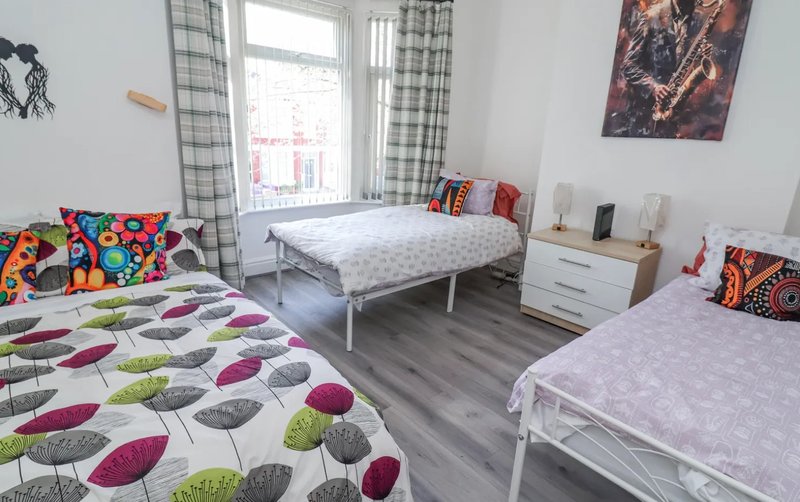 Bright shared bedroom with two single beds, colorful patterned bedding, wooden floor and window