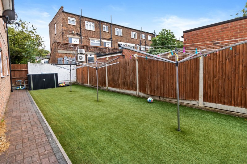 Rear garden with green lawn, wooden fence, clothesline, and brick apartment building