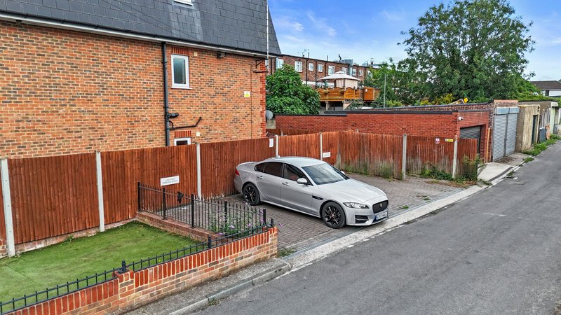 Brick house exterior with driveway, parked car, wooden fence and front garden