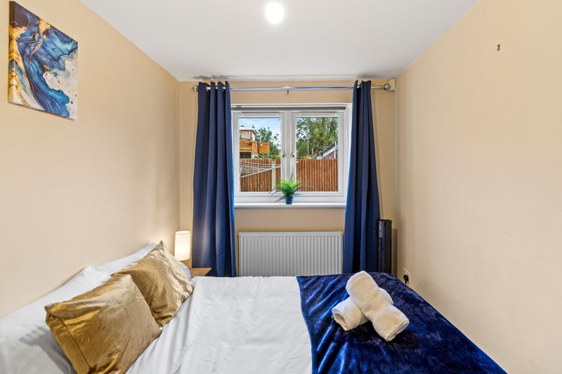 Compact bedroom with double bed, blue curtains, gold cushions and window view