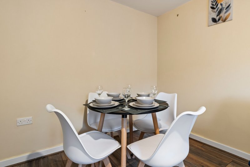 Dining area with round black table, two white chairs, place settings and wall art