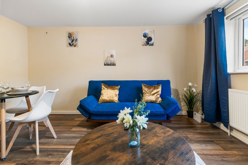 Open-plan living area with blue sofa, dining table, wooden flooring and bright window