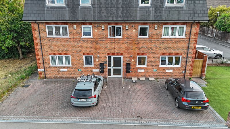 Brick apartment building with driveway, parked cars, and manicured front garden