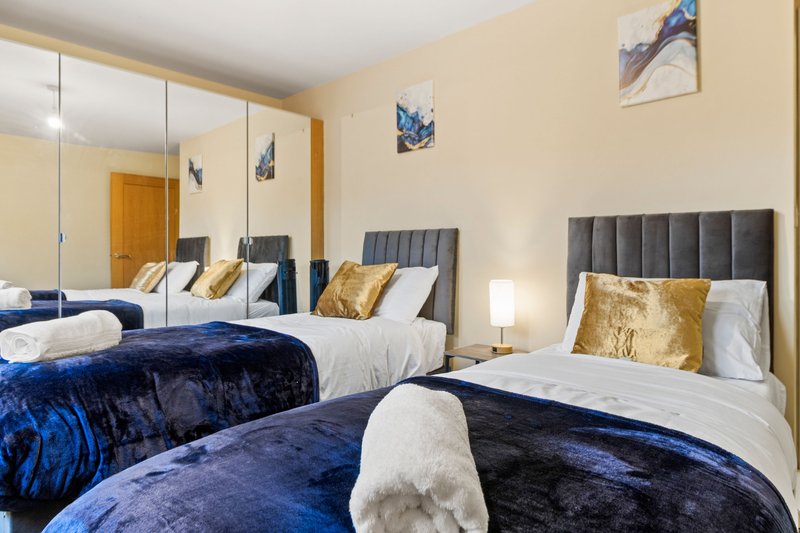 Twin bedroom with blue velvet bedding, padded headboards, gold cushions and mirrored wardrobe