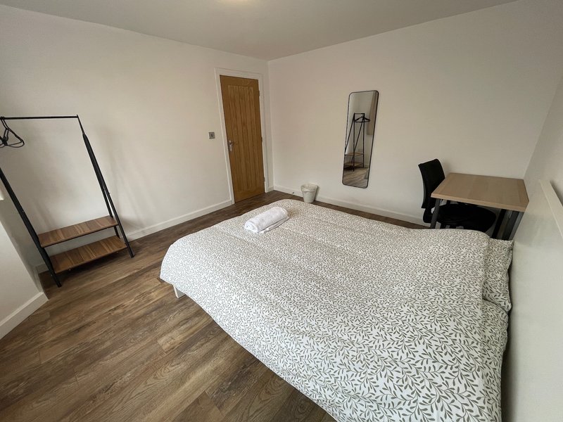 Spacious bedroom with double bed, wooden floor, desk, and wall-mounted mirror