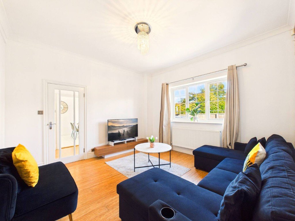 Bright living room with blue sofa, wooden floor, TV, and large windows with garden view