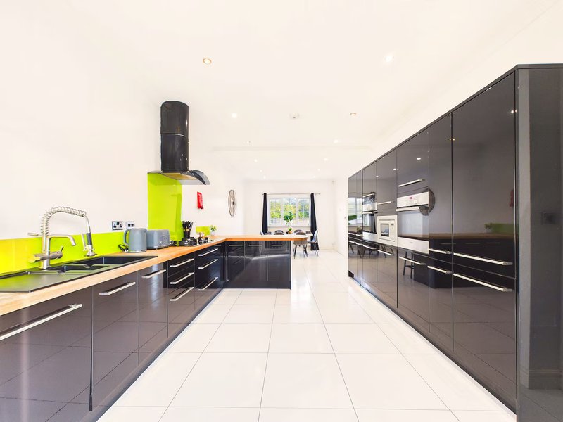 Modern kitchen with black cabinetry, yellow backsplash, stainless steel appliances and white floor tiles