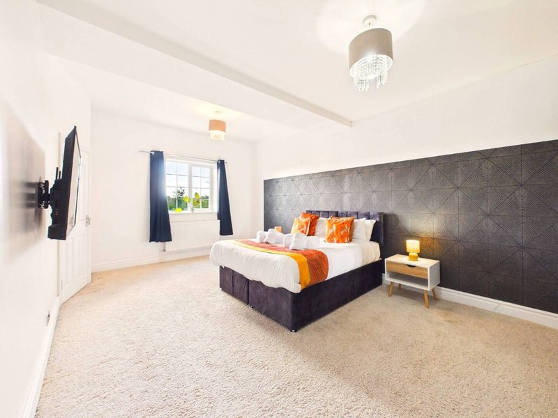 Bright bedroom with double bed, orange and purple bedding, dark feature wall, and window with blue curtains