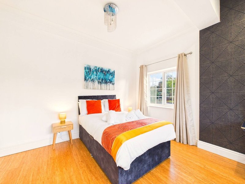 Bright bedroom with double bed, orange and yellow bedding, wooden floor and window