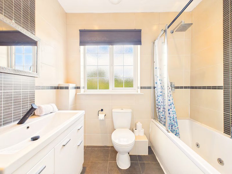Bright bathroom with white vanity, toilet, bathtub and window overlooking garden