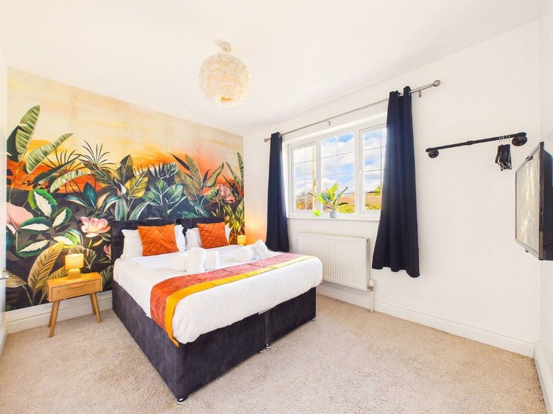 Bright bedroom with double bed, tropical wall mural, orange accents, and large window