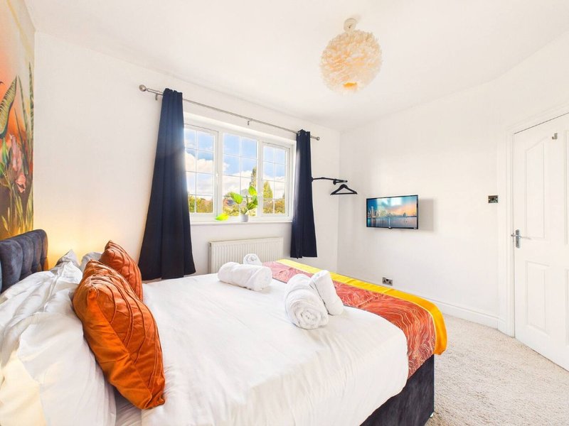 Bright modern bedroom with double bed, orange cushions, black curtains and window view