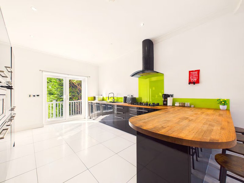 Modern kitchen with bright lime-green backsplash, wooden counter, black cabinetry and door to garden