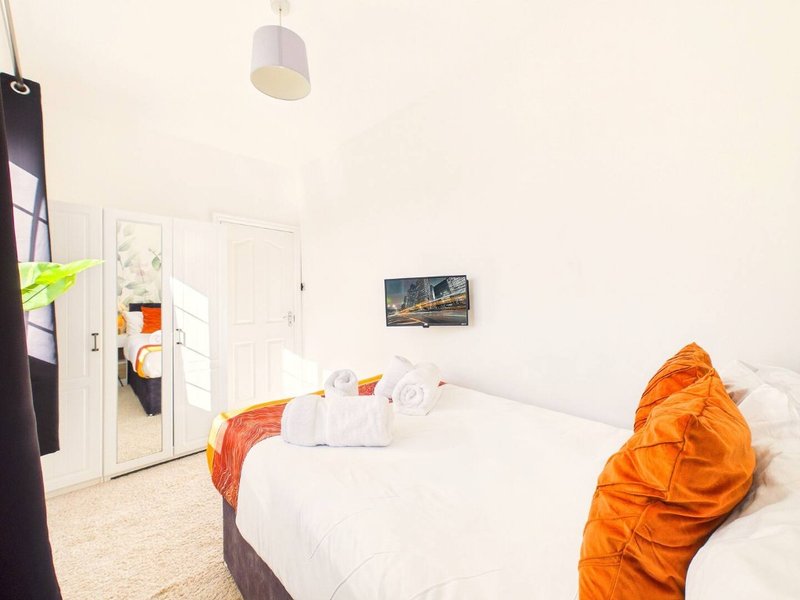 Bright bedroom with double bed, white bedding, orange throw, and door to ensuite bathroom