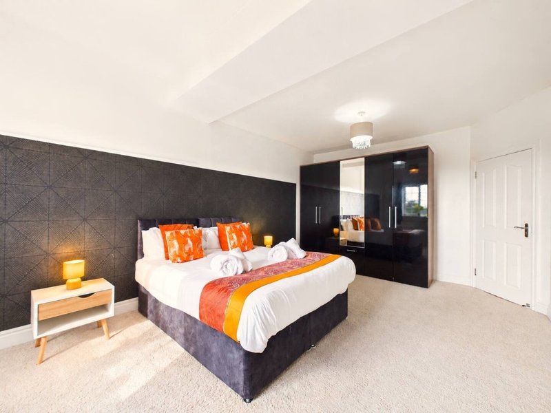 Modern bedroom with double bed, orange bedding, dark headboard, wooden nightstand and wardrobe