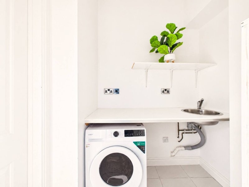 Compact utility room with washing machine, small sink and shelf with potted plant