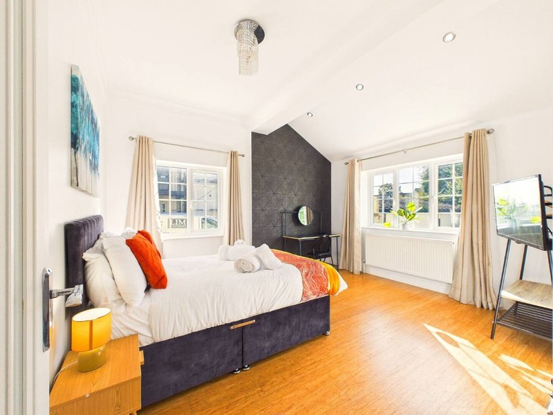Bright bedroom with double bed, dark headboard, wooden floor and multiple windows